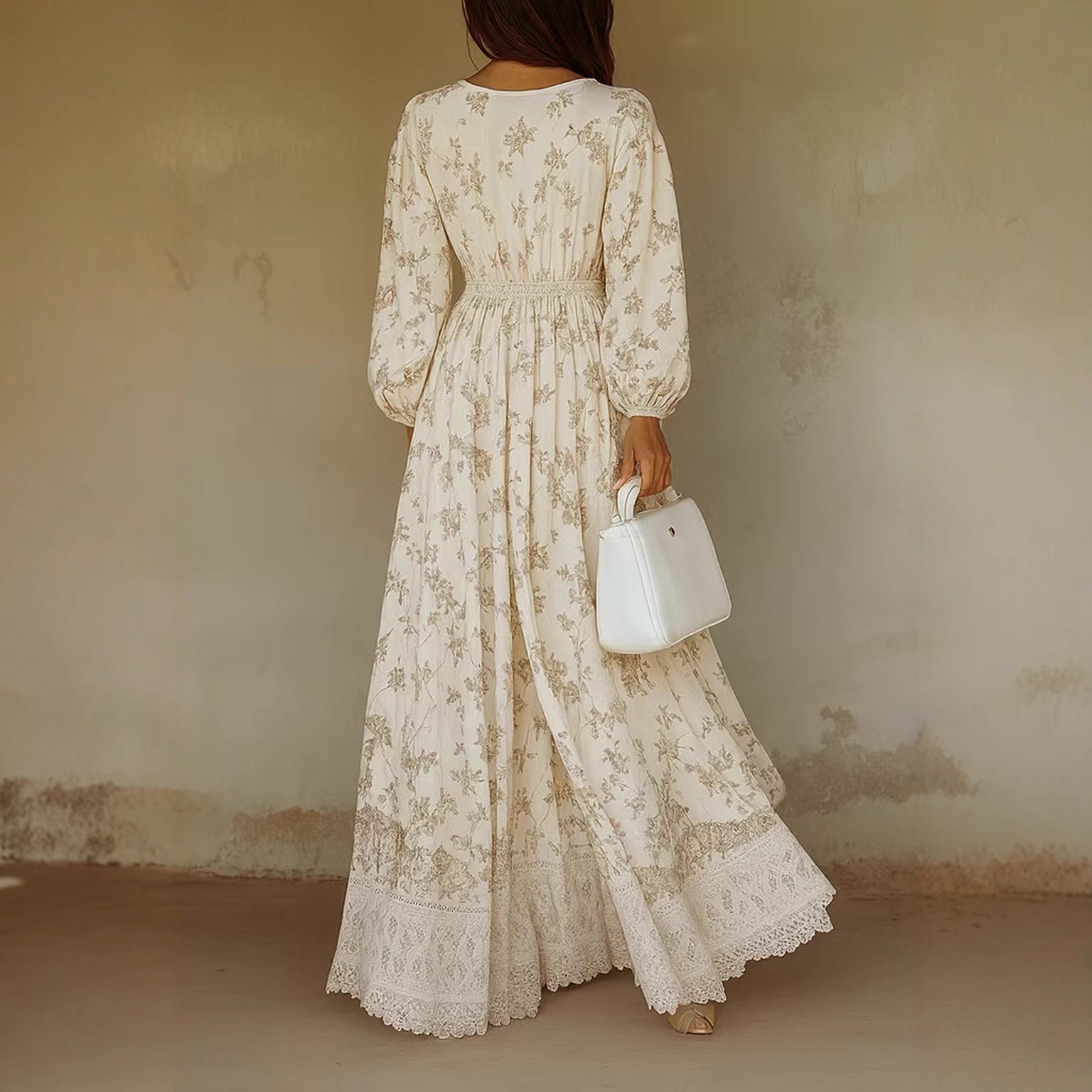 Woman wearing a long, floral lace dress against a plain wall.