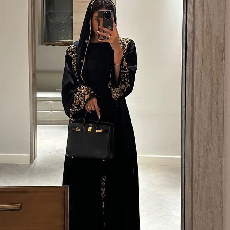 Person wearing a black outfit with gold embroidery holding a black handbag in a mirror selfie.