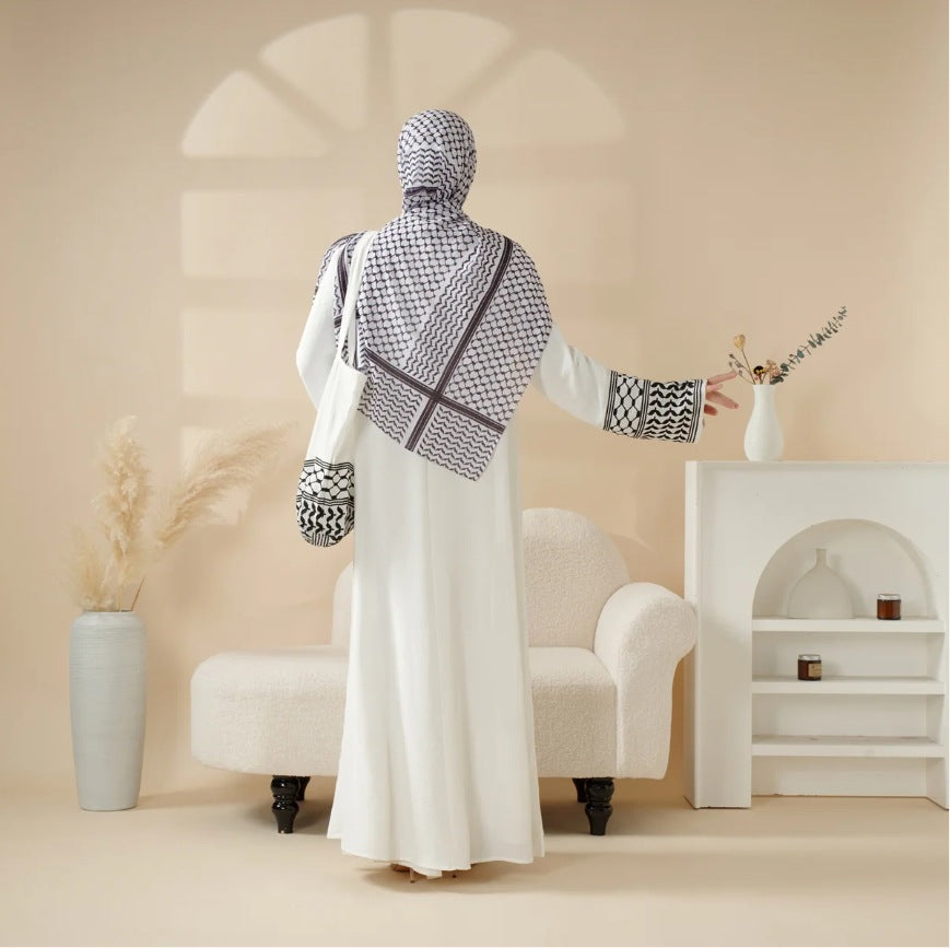 Person wearing a white dress with a patterned hijab in a minimalistic room.