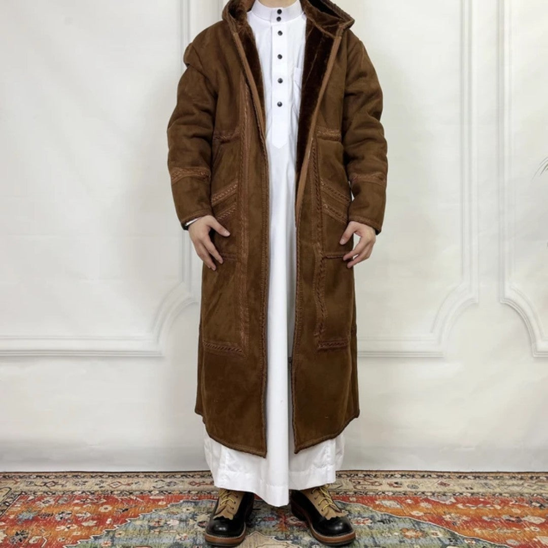 Person wearing a long brown coat over a white outfit on a decorative rug.
