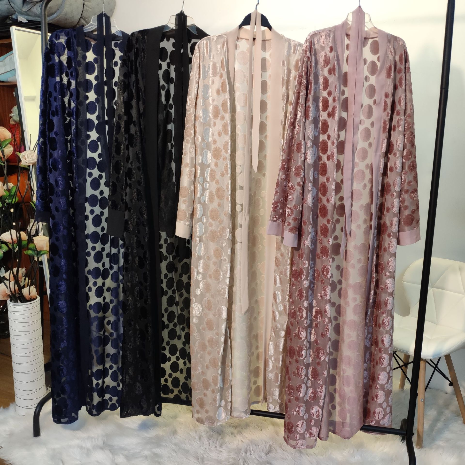 Four patterned dresses hanging on a rack with a chair and plant in the background.