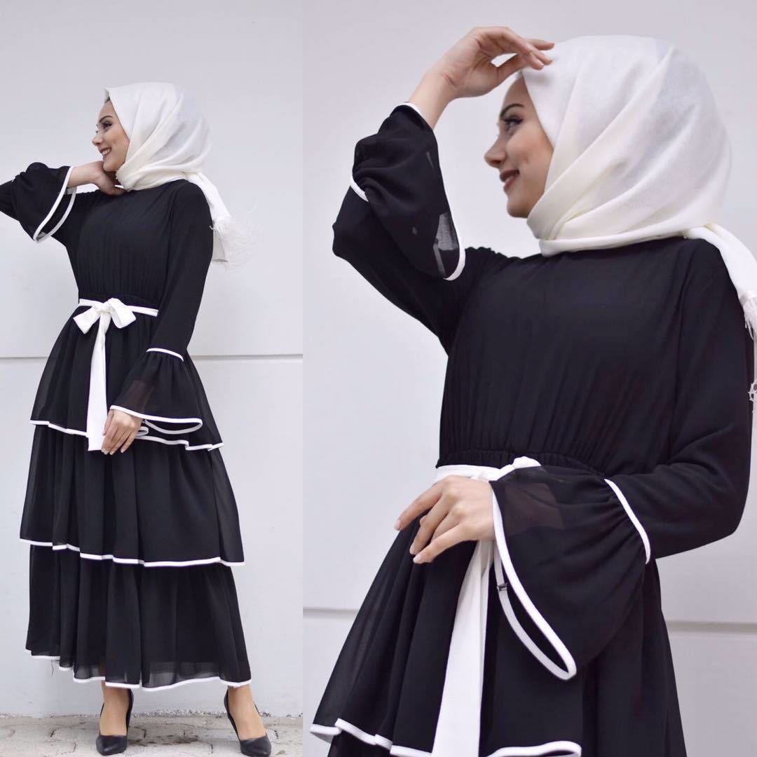 Woman wearing a black dress with white accents and hijab against a white background