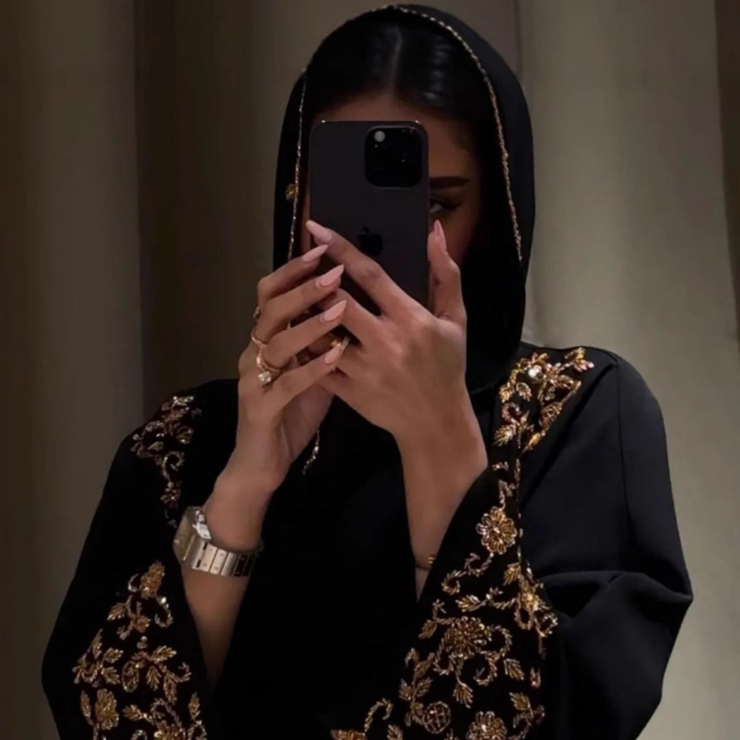 Woman in black embroidered outfit using a phone in a mirror.