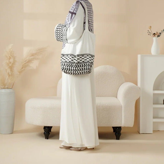 Person wearing a white outfit with a black and white patterned headscarf and bag in a room with beige walls and white furniture.
