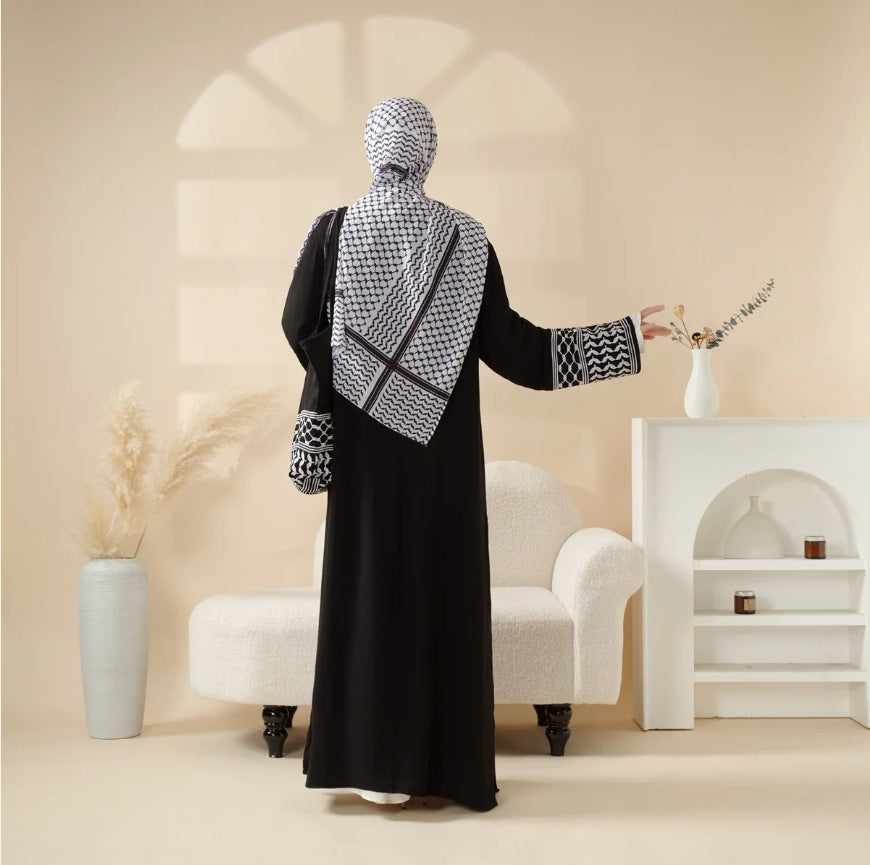 Person wearing a black abaya with a patterned scarf in a minimalistic room.